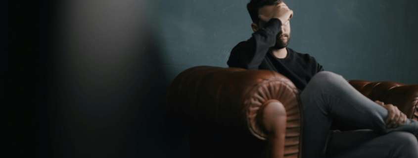 Anxious man sitting on a leather sofa holding his head.