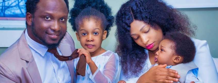 A black family with a baby and 5 year old sit for a portrait on a sofa. Families all have their own unique joys and stressors.