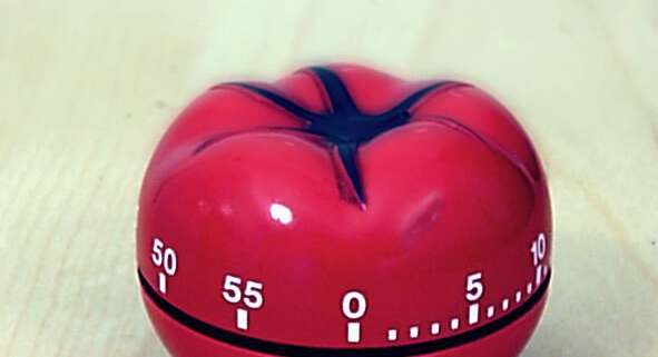 A red tomato kitchen timer sitting on a wood table.
