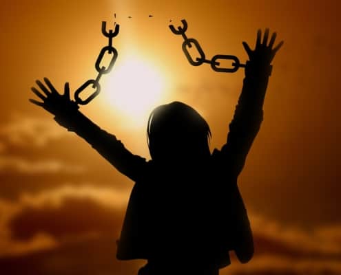 A silhouette of a person breaking out of the chains of adversity with the sunset in the background.