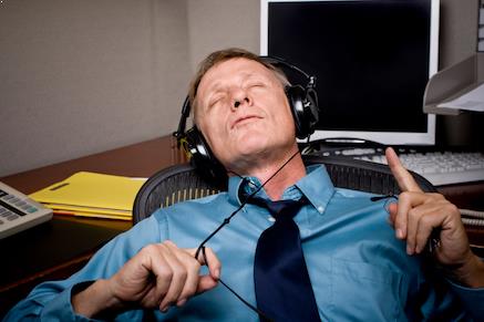 A man at his desk procrastinating by listening to music in headphones