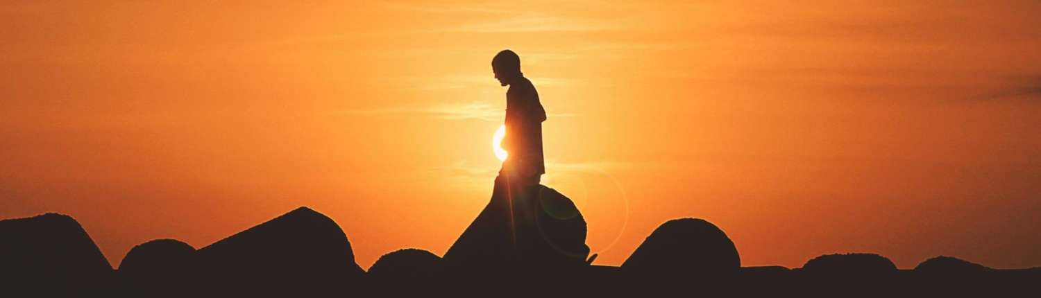 A silhouette of a person meditating at sunrise while seated on a rock.