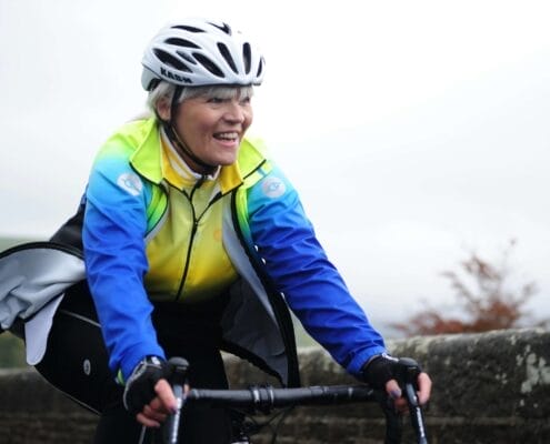 An older smiling woman confidently riding her bike in the fall.