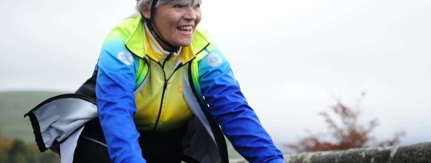 An older smiling woman confidently riding her bike in the fall.