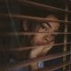 Socially Anxious woman looking through blinds wishing she was outside with other friends.