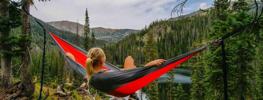 A woman hanging in a hammock in beautiful mountains with a river below her. Getting outdoors helps you reduce stress.