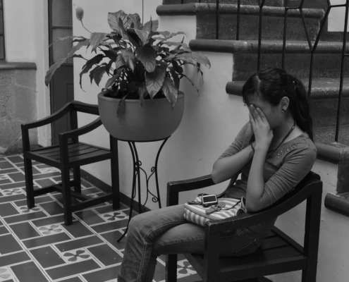 Picture of a teen girl crying in a chair in front of stairs in a beautiful home.