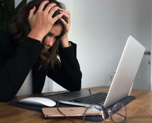 A woman in a black shirt holds her head in exasperation while looking at work on her laptop.